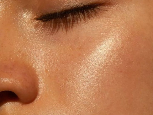 Close-up of a person's face with a focus on the cheek and closed eye, highlighting smooth, radiant skin with a sunlit glow.