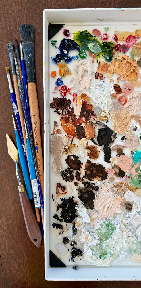 Picture of an oil paint palette with oil paint on it and brushes next to the palette