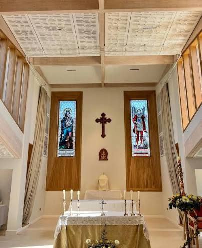 Interior of a bright modern church with altar, crucifix, and stained glass windows