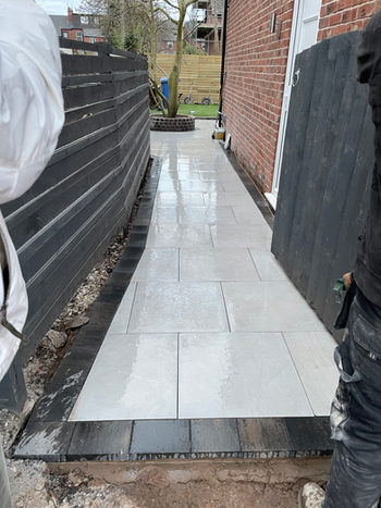New stone pathway installation with black borders and wooden fence background Artisan Landscaping