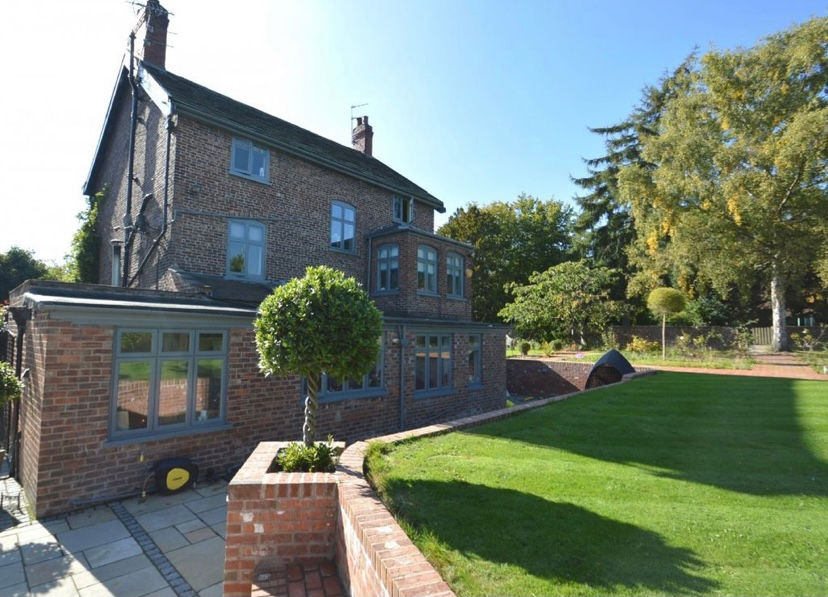 Large brick house with manicured lawn, windows, and surrounding trees.