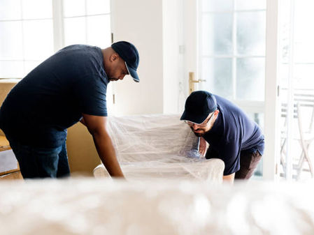 Two movers wrapping and lifting a chair during a home move.