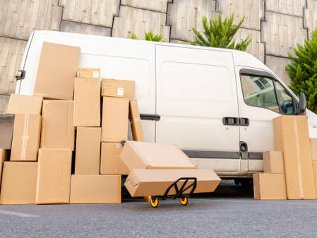 White delivery van with stacked cardboard boxes and a hand truck outside.