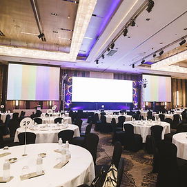 Large conference room with round tables, set up in front of three large projectin screens.