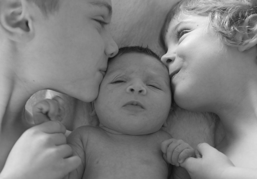 A black and white photo of my two sons on either side of my baby daughter, they are both kissing her head.