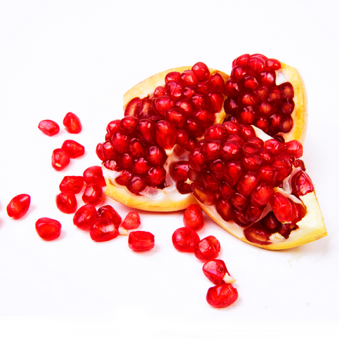Fresh pomegranate fruit cracked open with vibrant red seeds scattered across a white background, used to craft pomegranate botanical glycerite for skincare
