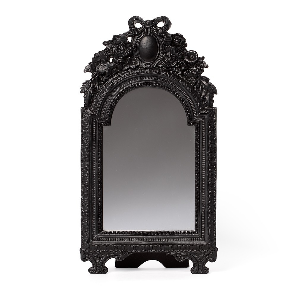 An elegant Victoriana mirror framed in richly detailed gothic ornamentation. The bow detail, arched design and antique black finish lend a sense of drama and depth, making it ideal for dark interiors, vanity spaces, or statement wall decor. Crafted from resin, this decorative mirror reflects both light and shadow, embodying timeless gothic romance. • Decorative gothic mirror with ornate Victoriana frame • Arched design with intricate antique-style and bow detailing • Ideal for wall display, vanity styling, or statement decor • Reflective glass set within a durable resin frame • Perfect for gothic, vintage, or alternative interiors • Adds depth, light, and dramatic atmosphere to any space • Free-standing or wall hung Colour: Black