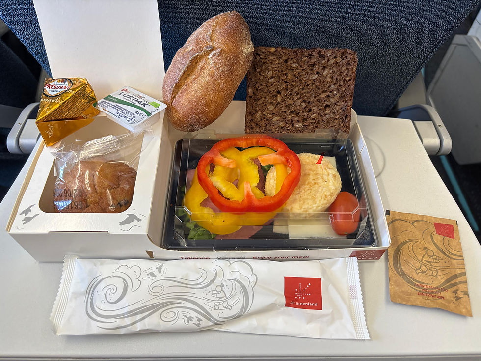 Plateau-repas ouvert à bord avec une sélection de pain, de légumes frais, de fromage, de beurre, un muffin, et des couverts qualitatifs.