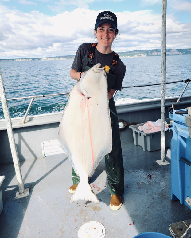 Woman holding a large halibut aboard a fishing boat off the coast of Alaska.