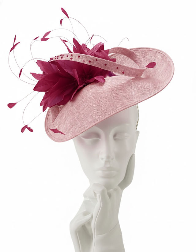 Two bespoke pink wedding hats displayed side by side — a bold fuchsia fascinator with silk flower and a soft blush wide-brim saucer hat, both designed by Marvellous Millinery, Winchester