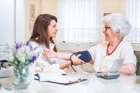 Older woman getting blood pressure measured by nurse while seated at kitchen table
