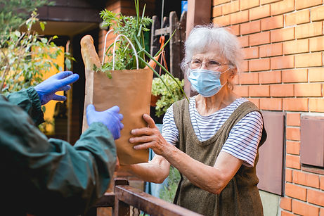 Older woman wearing mask accepting a bag of groceries outside of her house
