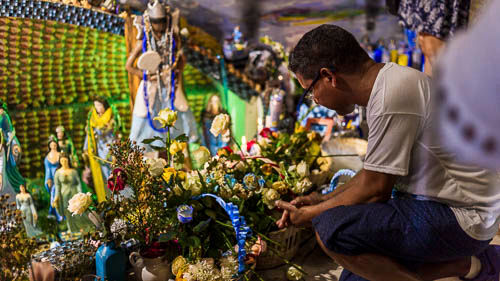 homem agachado no barracao de yemanja a noite e muitas flores ao redor