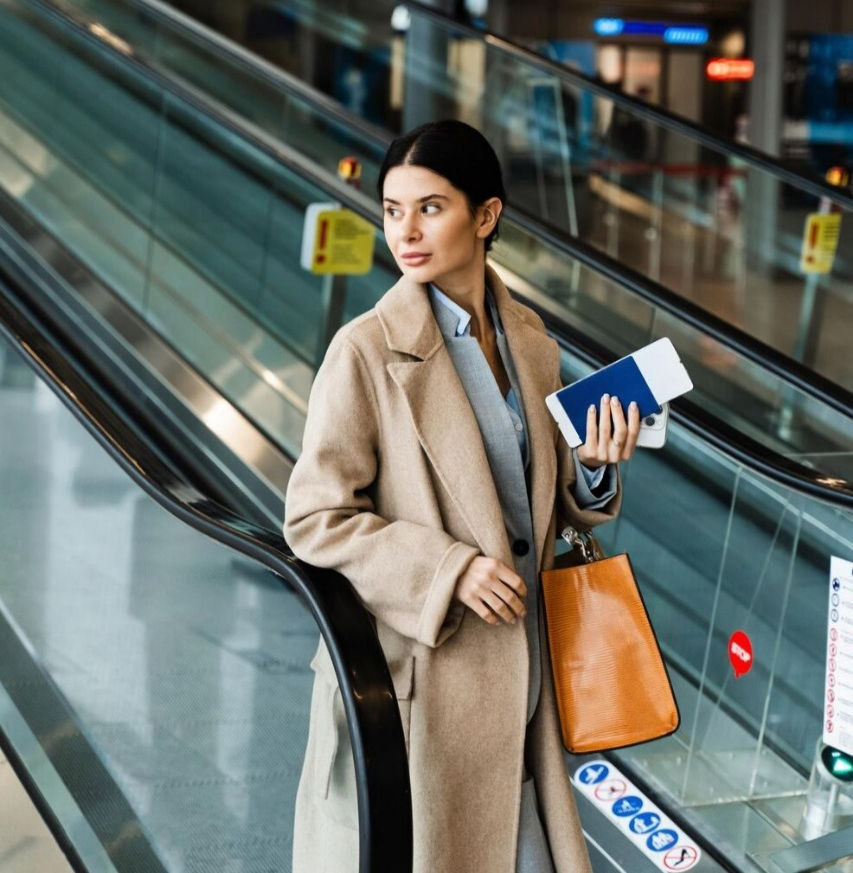 traveler-holding-boarding-pass-passport-smartphone-handbag-while-standing-near-escalator-a