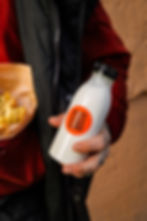 Nahaufnahme einer Person in einer rot-schwarzen Jacke, die Pommes und einen selbstgemachten Ayran im „Kebap with Attitude“ in Berlin in der Hand hält.