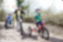 Three smiling children riding bikes and trikes