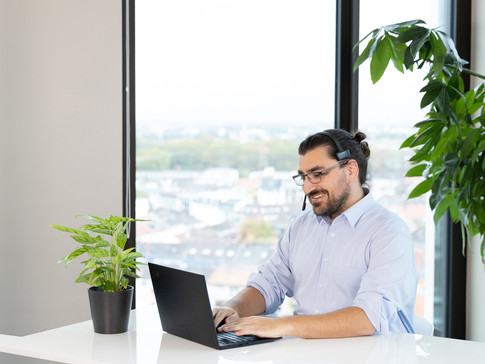 Mann mit Headset sitzt am Laptop in Büroumgebung Businessportrait