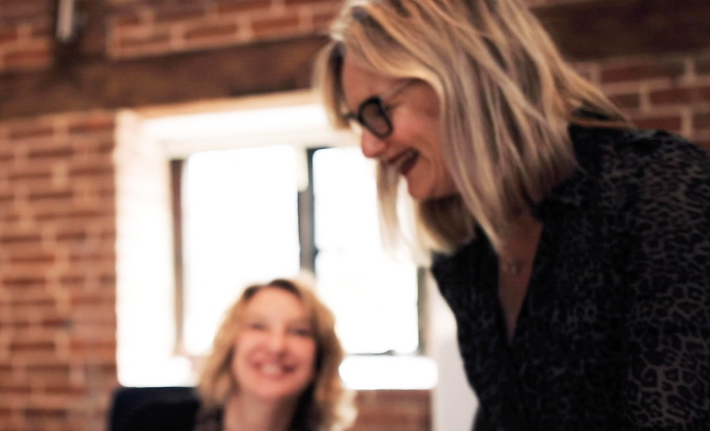 A picture of Wise Bird Marketing Founders Sascha Way and Jo Sutherland working together two women in an office laughing and chatting