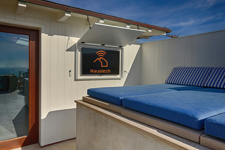 Outdoor balcony featuring a blue cushioned lounge bed and a television folding down from a weather-protective overhead enclosure, Hermosa Beach Haven.