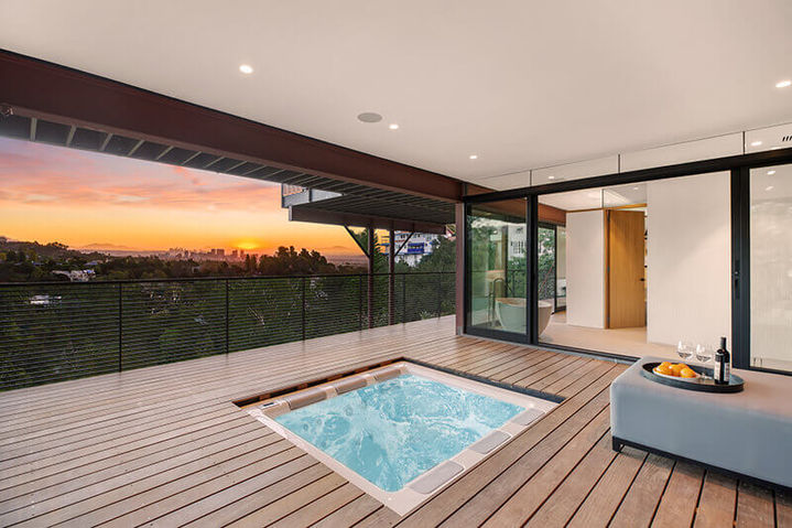 Covered outdoor wooden deck featuring a square built-in hot tub, glass railings, and a sunset view over the hills, Westridge Hillside Retreat.