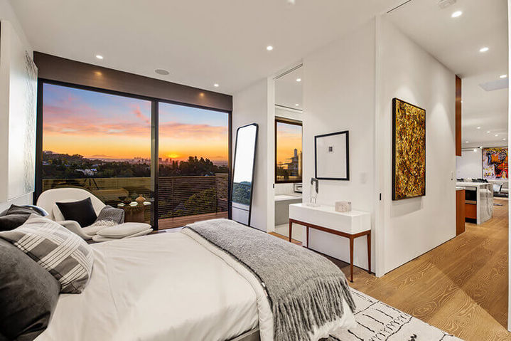 Bedroom featuring a white bed, a large floor mirror, and floor-to-ceiling windows displaying a sunset view, Westridge Hillside Retreat.