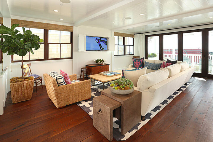 Open living area with dark wood floors, a large white sectional, a wicker armchair, and a wall-mounted television, Hermosa Beach Haven.