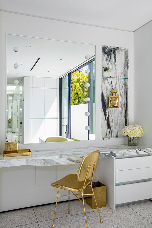 Bright vanity area featuring a large mirror, white counter, gold chair, and a glass door opening to greenery, Beverly Hills Party Pad.