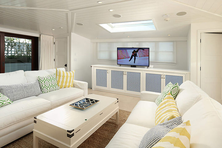 Bright white living room featuring two facing sofas, a central coffee table, and a wall-mounted television above a cabinet, Hermosa Beach Haven.