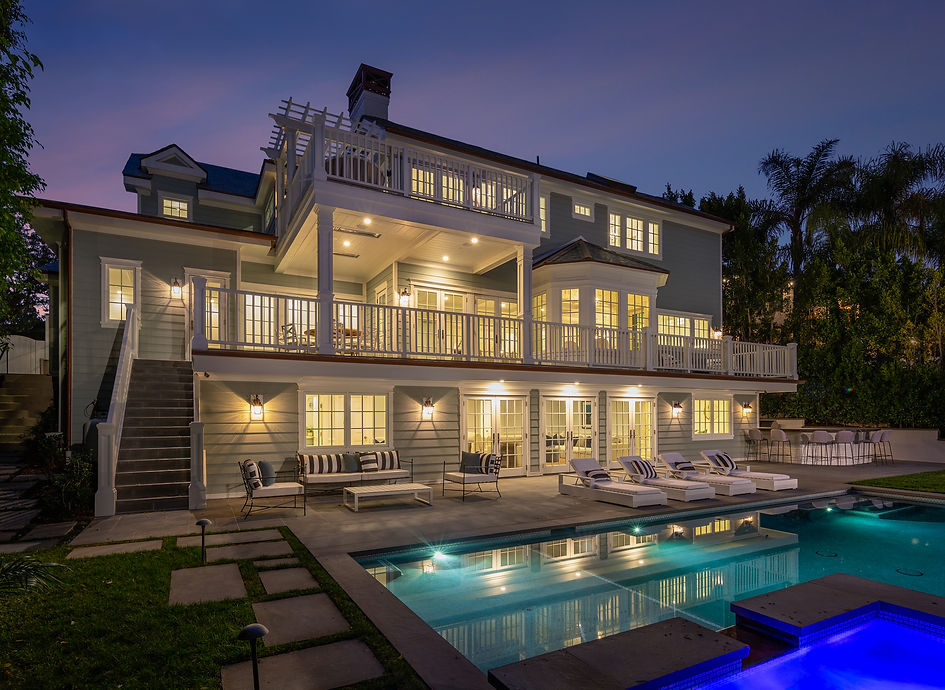 A dusk view of the rear of the home, showcasing the pool and lush backyard