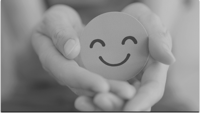 A greyscale image of a smiley face emoji being held in some ones hands.