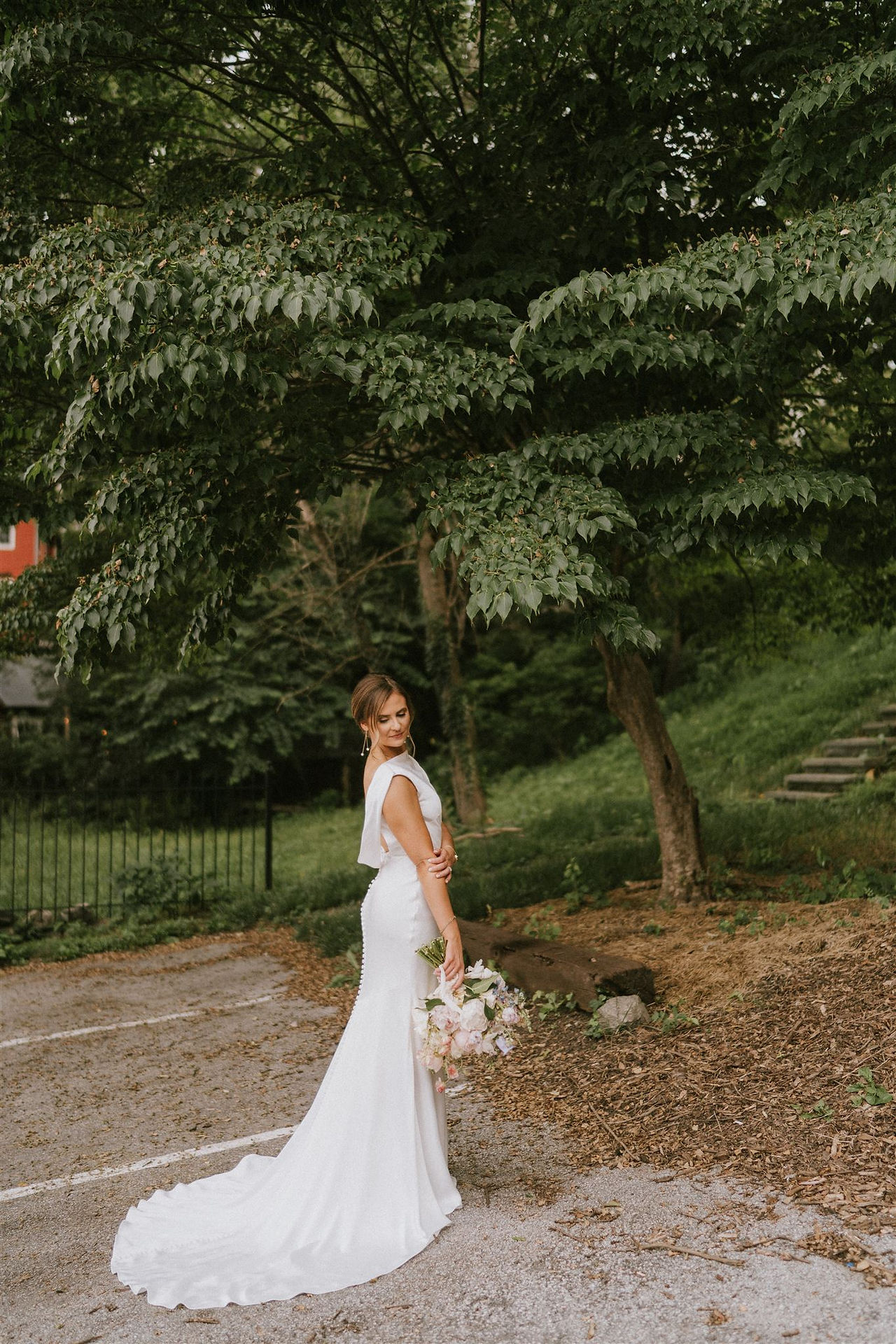 a bride stands showing the back of her low cut dress and bouquet