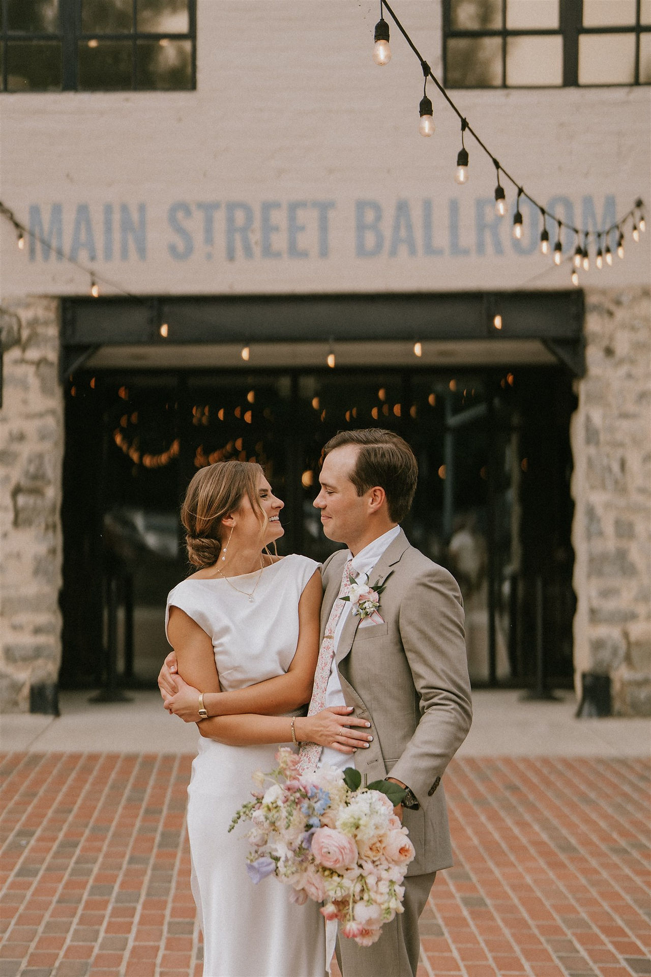 a bride and groom stand close, smiling at each other