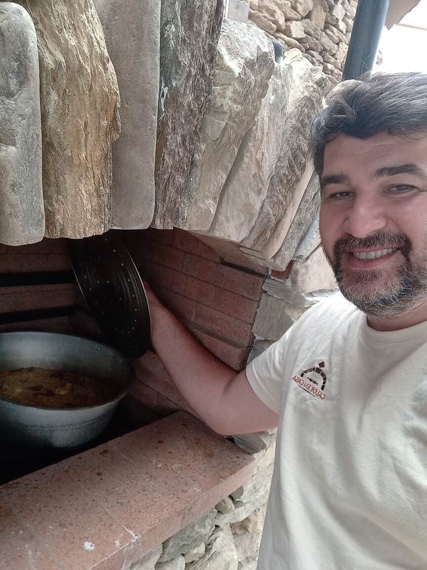 Hombre sonriente frente a horno con plato. Estufa calefactora con horno. Segovia, octubre de 2022. Calor En Casa.