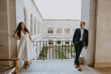 Couple standing by a balcony, smiling and looking out at the gardens.