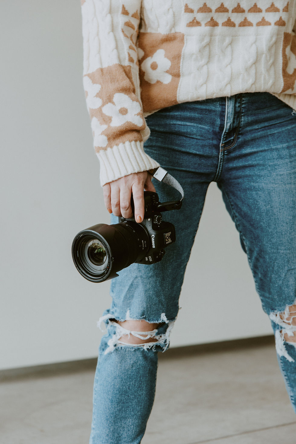 A photographer in a cozy knit sweater and ripped jeans holds a camera, ready to capture moments.