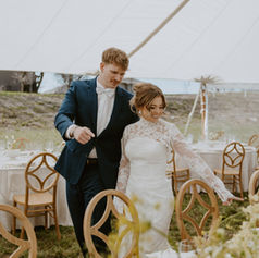 Bride and groom walk near tables; Weddings, elegant outdoor reception setting.