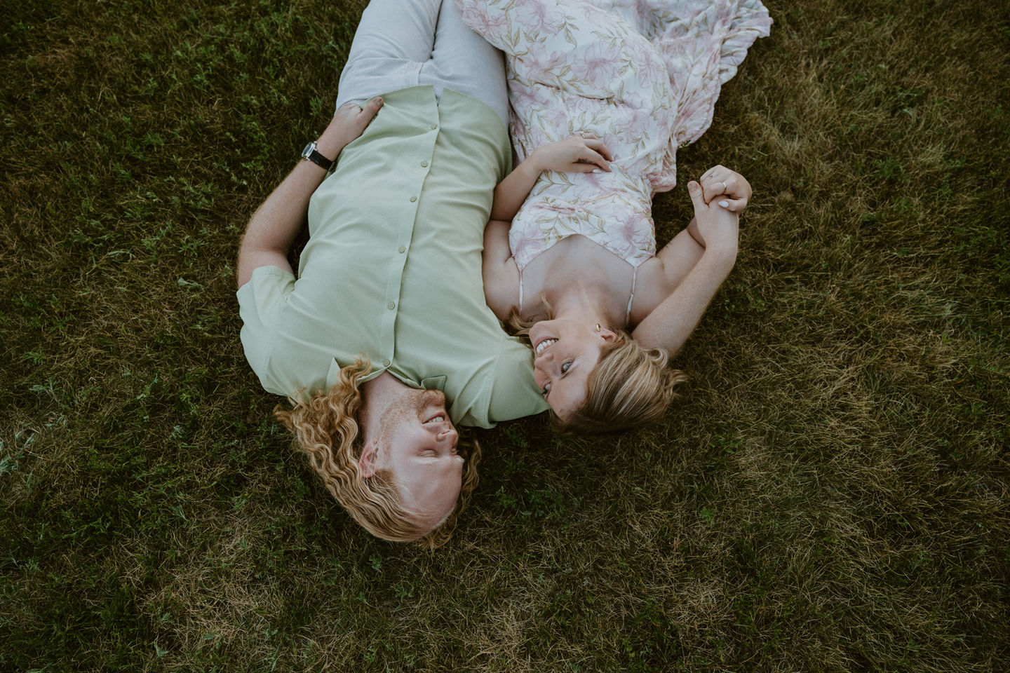 Couple lying on grass, laughing, holding hands in a park, happy moment