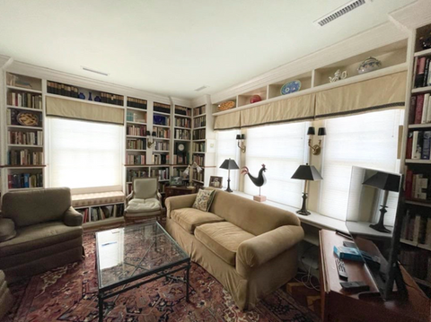 A cozy sunroom and home library featuring extensive built-in bookshelves and windows with custom flat Roman shades, offering a blend of comfort and style. Design and installation by Mill End Shops