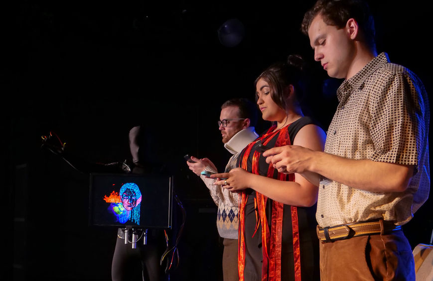 Actors stand on a stage in end bows, on their phones in a metaphorical gesture.