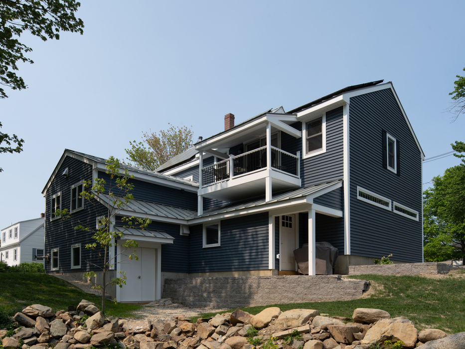 Dark blue house with white trim, a balcony, and rock landscaping.
