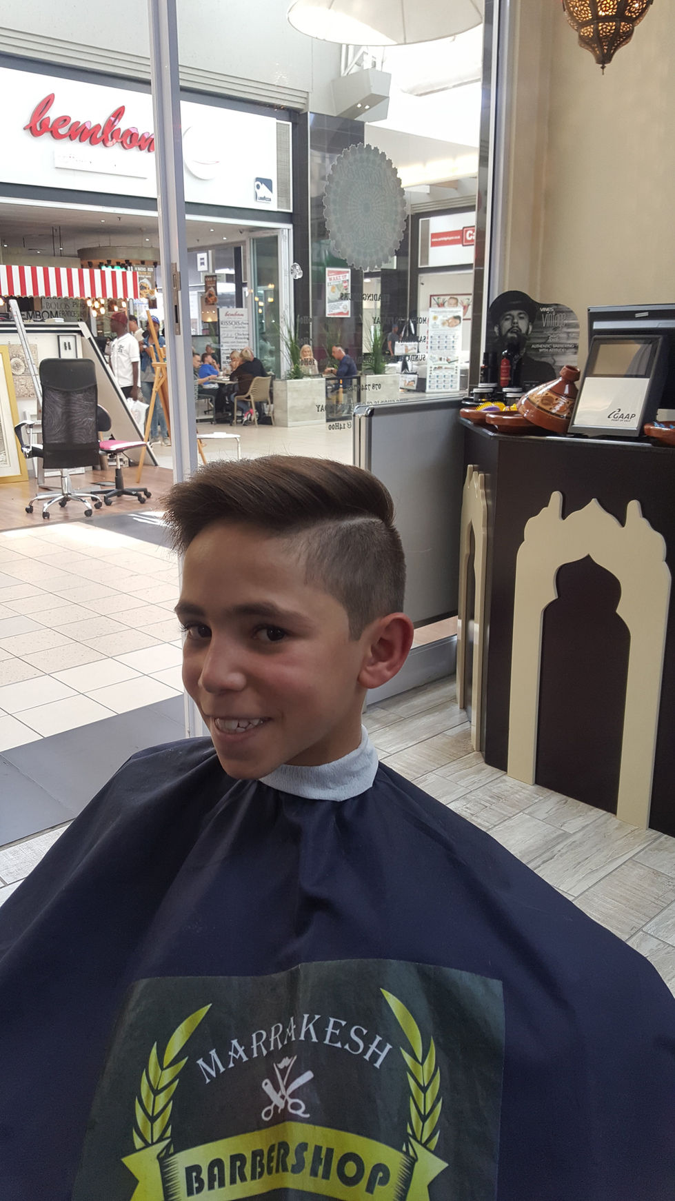 Young boy with new haircut, Marrakesh Barber Shop logo and smiling face Marrakesh Barber Tm