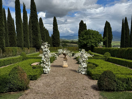 Allestimento floreale per elopement nel giardino all'italiana di Tenuta Argiano, Montalcino — colonne di gigli bianchi sul vialetto con cipressi e Val d'Orcia sullo sfondo