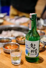 a-bottle-of-jinro-chamisul-soju-on-a-table-with-food.webp