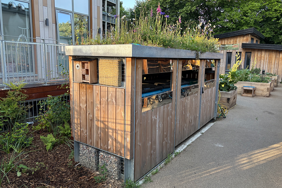 Metal frames binstore with larch timber cladding sits in a housing block with planted beds and trees around it.