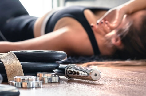 Eine Sportlerin, die komplett erschöpft neben ihrem Trainingsequipment liegt.