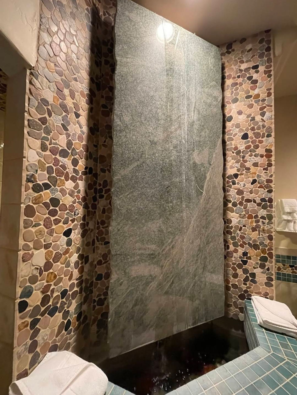 a bathroom with a stone wall and a mosaic rock waterfall tile
