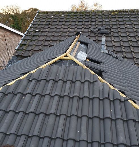 Close-up of a rooftop with dark grey shingles, partially replaced with new tiles over a wooden framework