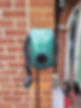 A green EV charging port on a brick pillar outside a home
