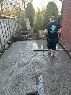 Man leveling wet concrete in backyard; construction in progress, sunny weather.