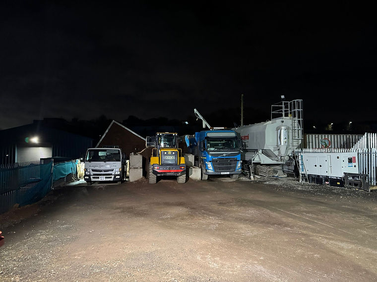 Construction site at night with trucks and heavy equipment. Dark scene.